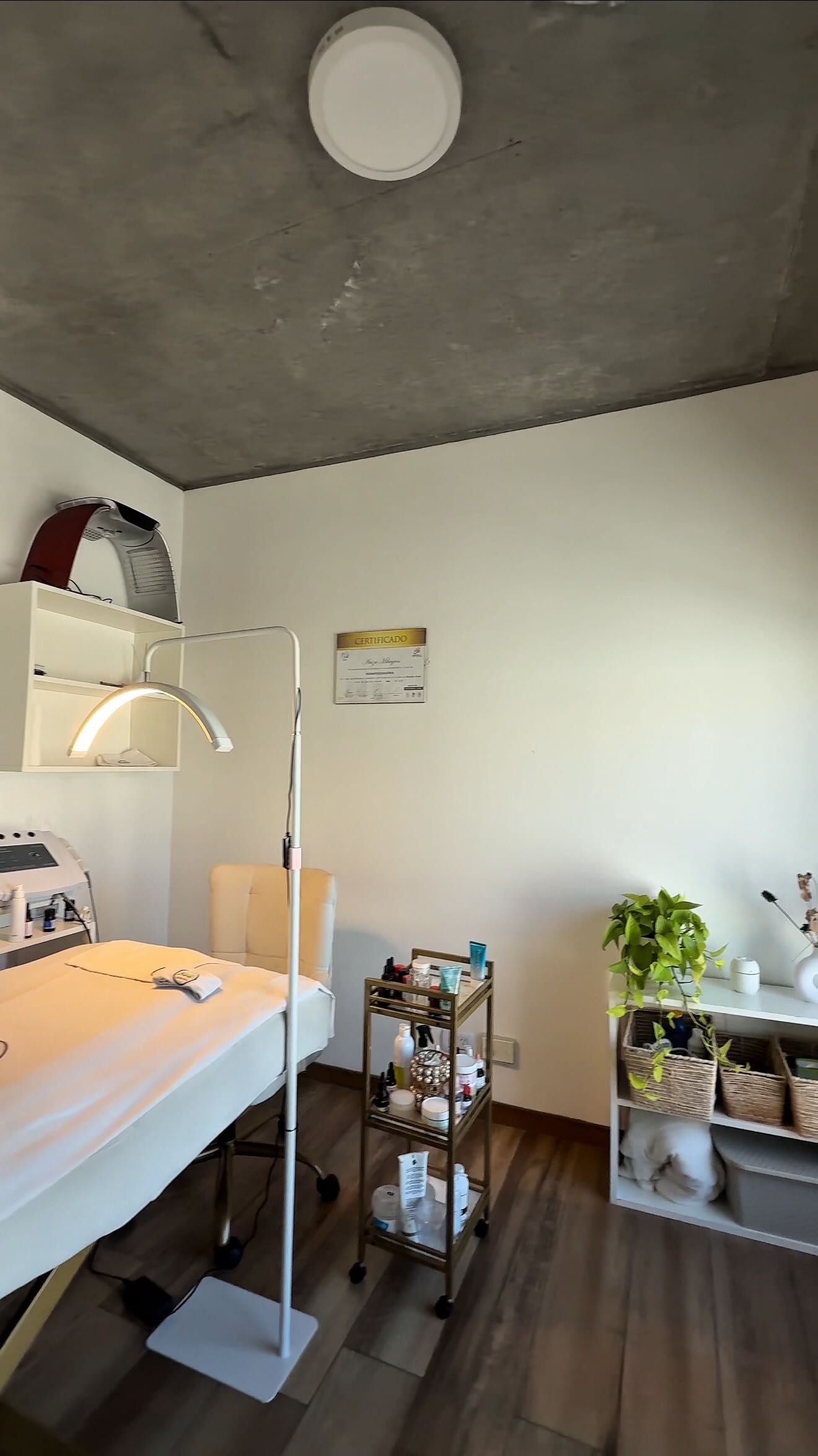 Una cabina de ByH Estética: la camilla, la lámpara de arco, la cabina LED en el estante y el carrito dorado con activos